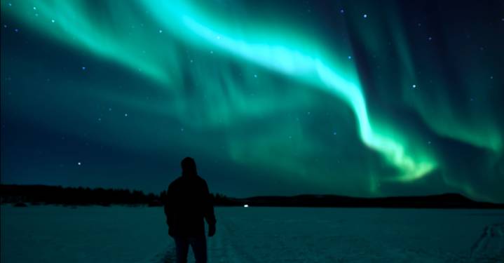 A man looking at northern lights on the frozen lake